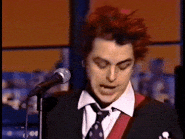 a man with red hair is singing into a microphone while wearing a suit and tie