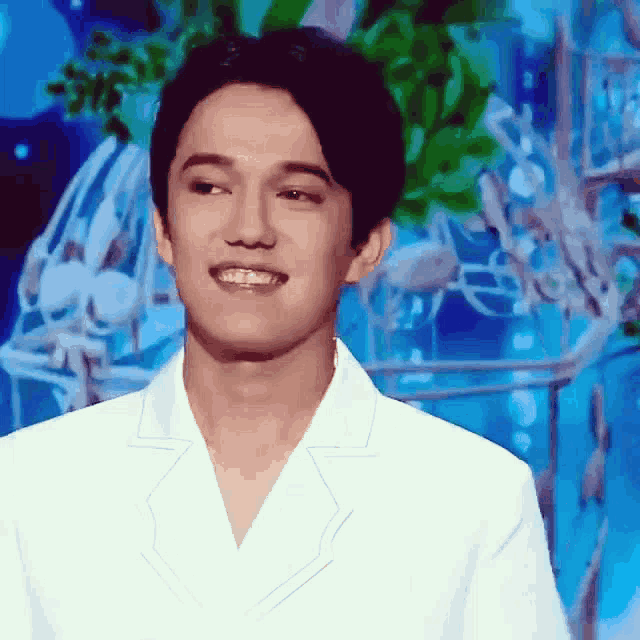 a man in a white jacket is smiling with a blue background behind him