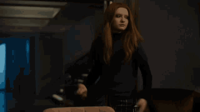 a woman with red hair is standing in a dark room holding a purse .