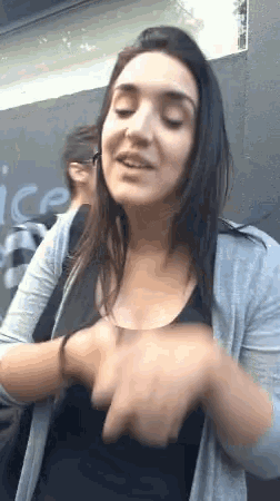 a woman wearing a black tank top and a grey cardigan is standing in front of a sign that says nice
