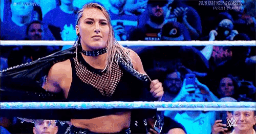 a woman is standing in a wrestling ring with a jacket on her shoulder .