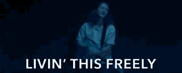 a man playing a guitar in a dark room with the words livin ' this freely below him