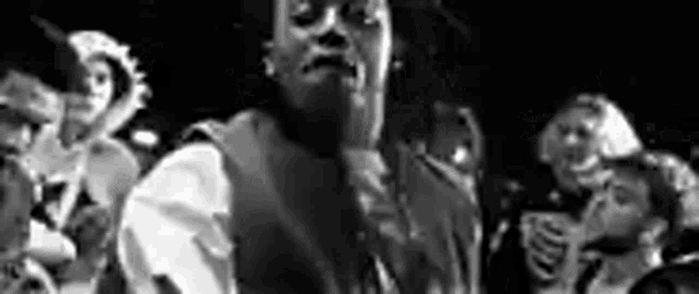 a black and white photo of a man standing in front of a microphone in a crowd .