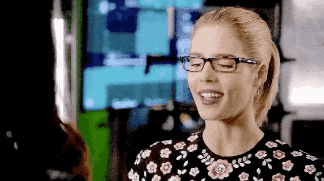 a woman wearing glasses and a floral shirt is smiling and looking at the camera .