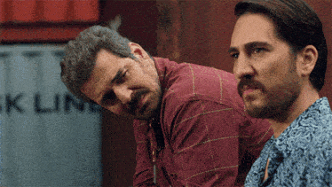 two men are looking at something in front of a container that says ' ck line '