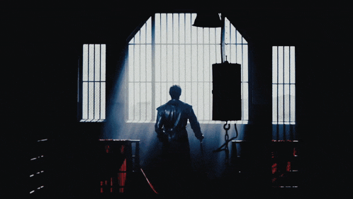 a man in a leather jacket stands in front of a window with bars on it