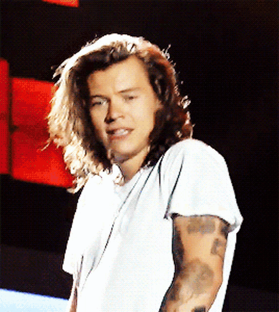 a man with long hair is wearing a white shirt with a tattoo on his arm