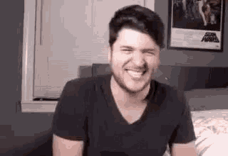 a man with a beard is sitting on a bed laughing .