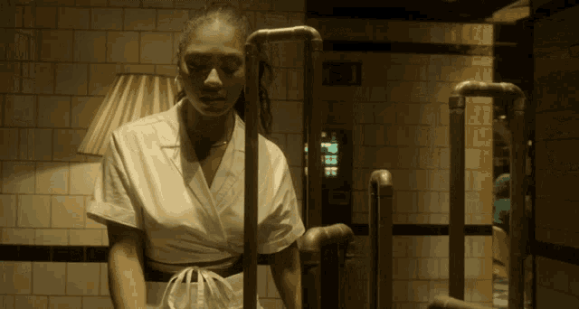 a woman in a white shirt is standing in a room with pipes and a lamp