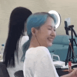 a woman with blue hair is smiling while sitting at a table in front of a camera .