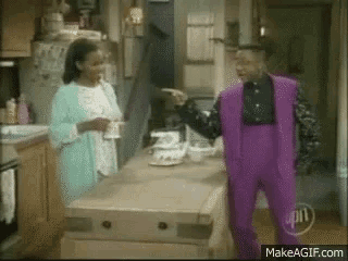 a man in purple pants is pointing at a woman in a kitchen