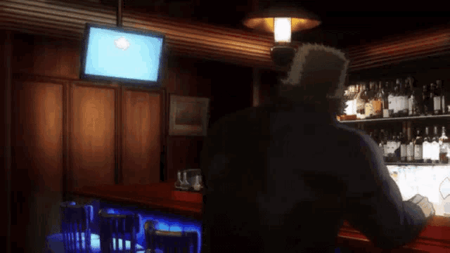 a man sits at a bar looking at a tv screen