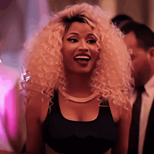 a woman with blonde curly hair is smiling and wearing a black tank top