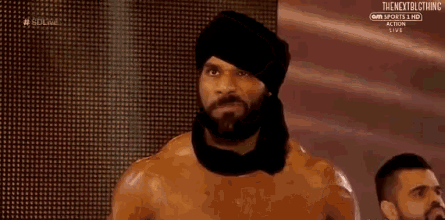 a man with a beard and a turban is standing in front of a crowd .