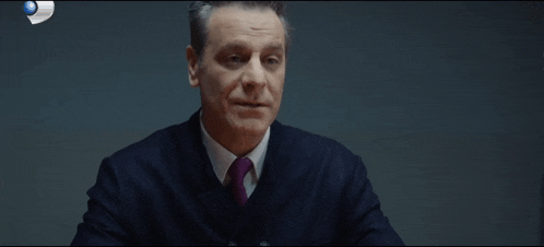 a man in a suit and tie is sitting in front of a sign that says ' televizyon ' on it