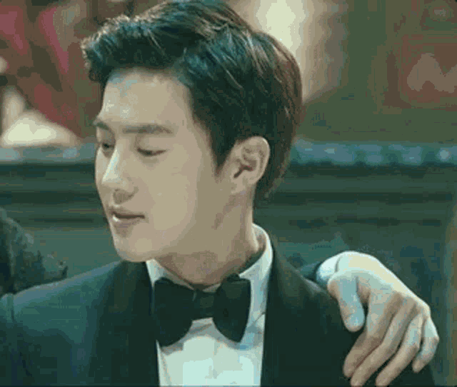 a man in a tuxedo and bow tie is being held by a woman 's hand .