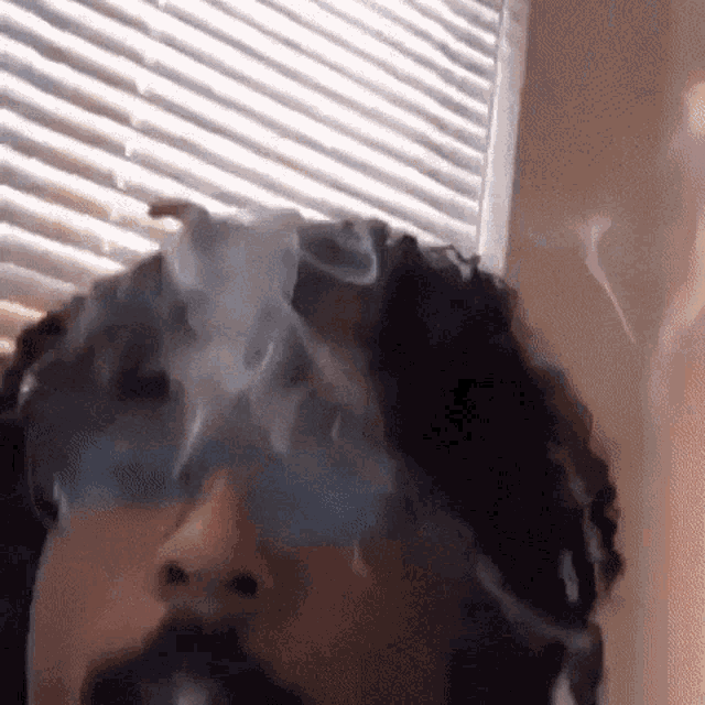 a person with dreadlocks is smoking a cigarette in front of a window .