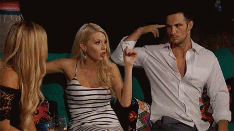 a man and two women are sitting on a couch and the woman is pointing at the man 's head