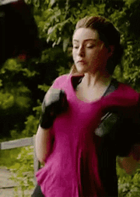 a woman in a pink shirt and black boxing gloves is running in the woods .