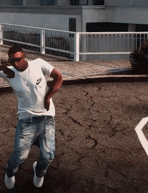 a man in a white nike shirt and blue jeans is dancing on a street .