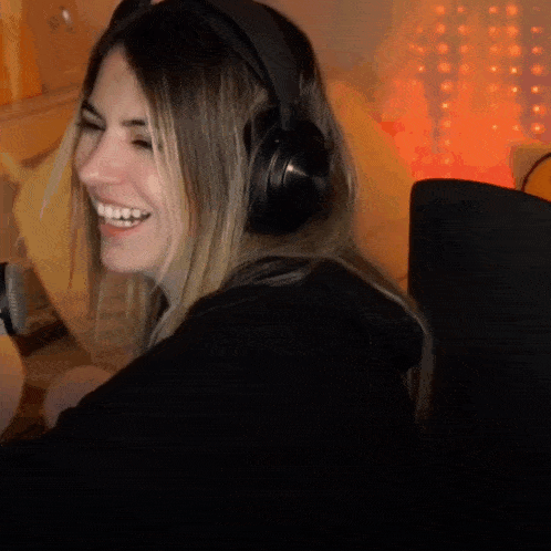 a woman wearing headphones is smiling while sitting in a dark room
