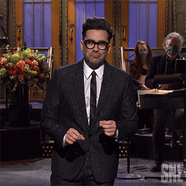 a man in a suit and tie stands in front of a sign that says ' snl '