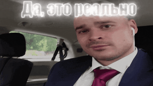 a man in a suit and tie is sitting in the back seat of a car with a sign above him that says да это реально
