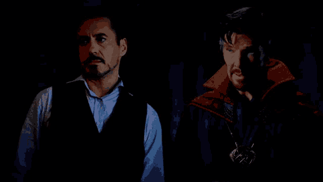two men standing next to each other in a dark room