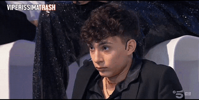 a young man in a black suit is sitting in front of a tv screen that says viperissimo trash