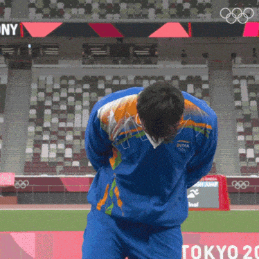 a man in a blue tokyo olympics jacket stands on a field