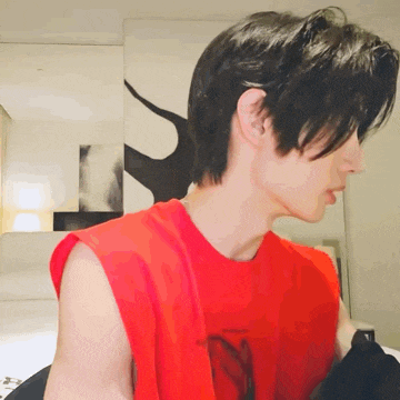 a man wearing a red sleeveless shirt is sitting on a bed .
