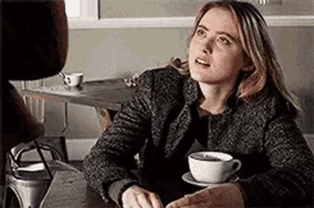 a woman is sitting at a table with a cup of coffee and a saucer .