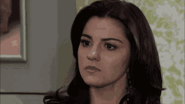 a woman with long dark hair is looking at the camera with a serious look on her face