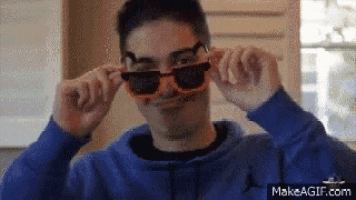 a man wearing a blue hoodie and orange sunglasses is making a funny face .