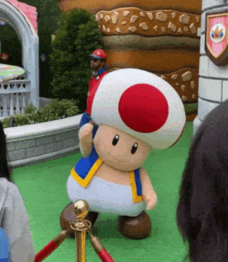 a man in a red hat is standing behind a toad mascot