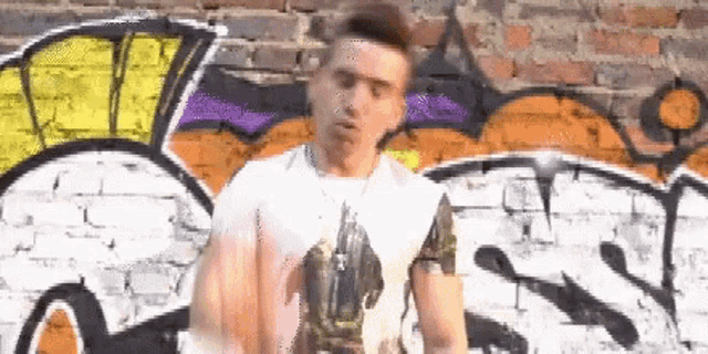 a man is standing in front of a graffiti covered brick wall .