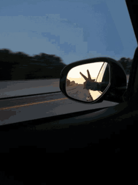 the rear view mirror of a car shows a person giving the peace sign