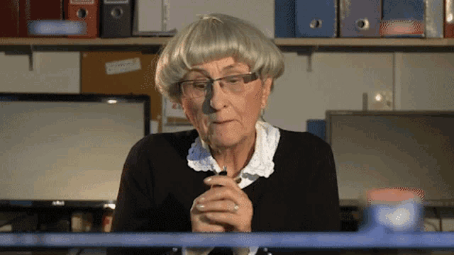 an older woman wearing glasses and a wig is sitting at a desk