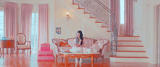 a woman is sitting on a pink couch in a living room with stairs .