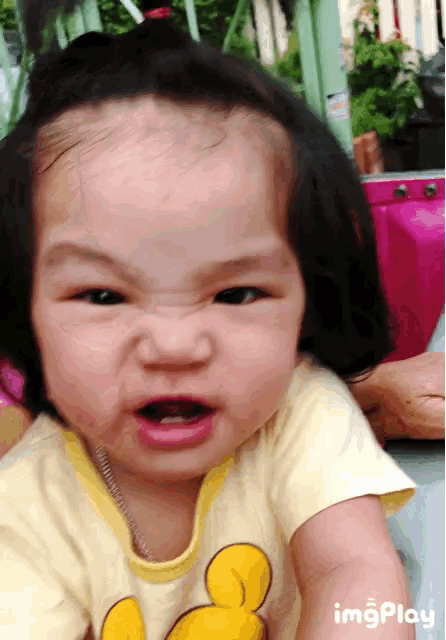 a baby girl wearing a yellow shirt with mickey mouse on it making a funny face