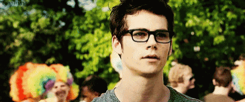 a young man wearing glasses and a gray shirt is standing in front of a crowd .