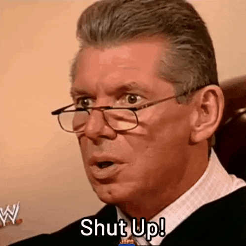 a man wearing glasses and a suit is sitting in a chair and saying `` shut up '' .