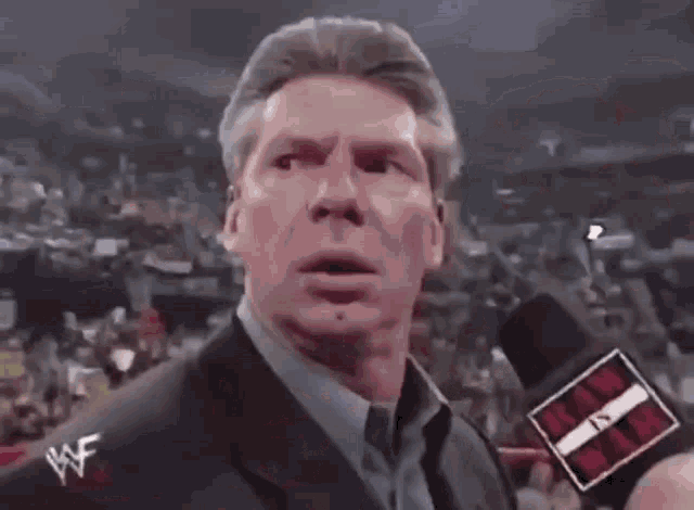 a man wearing a suit and tie is talking into a microphone with a wwe logo on it