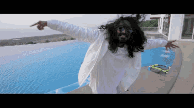 a man with long hair and a beard is standing in front of a pool with his arms outstretched