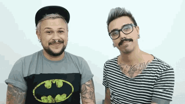 a man wearing a batman shirt stands next to another man with glasses