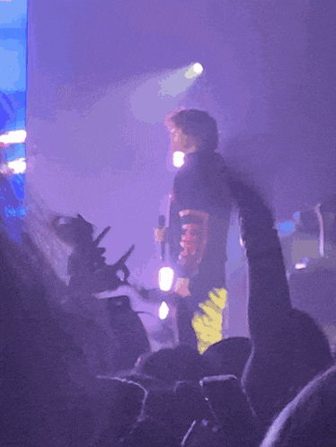 a man stands on stage with a microphone and a shirt that says ' supreme ' on the back