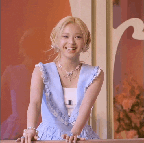 a woman wearing a blue dress and a necklace smiles for the camera