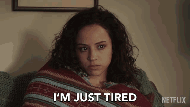 a woman wrapped in a blanket with the words i 'm just tired below her