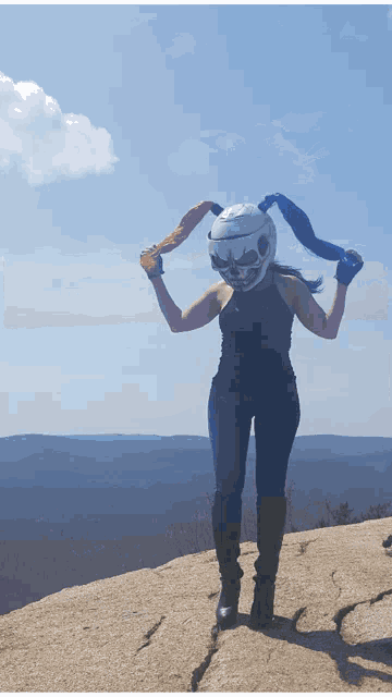 a woman wearing a helmet with a skull on it stands on a rock