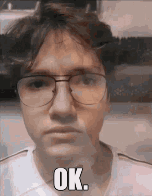a man wearing glasses and a white shirt with the word ok on his face